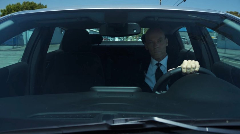 Enoch driving past an airport hangar.