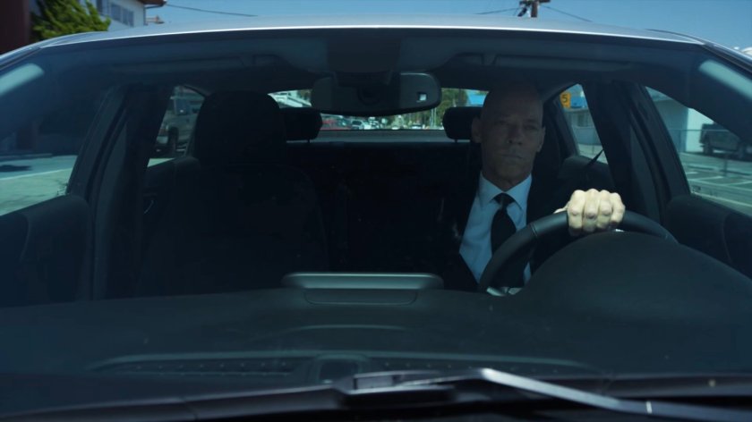 Enoch driving past an airport hangar.