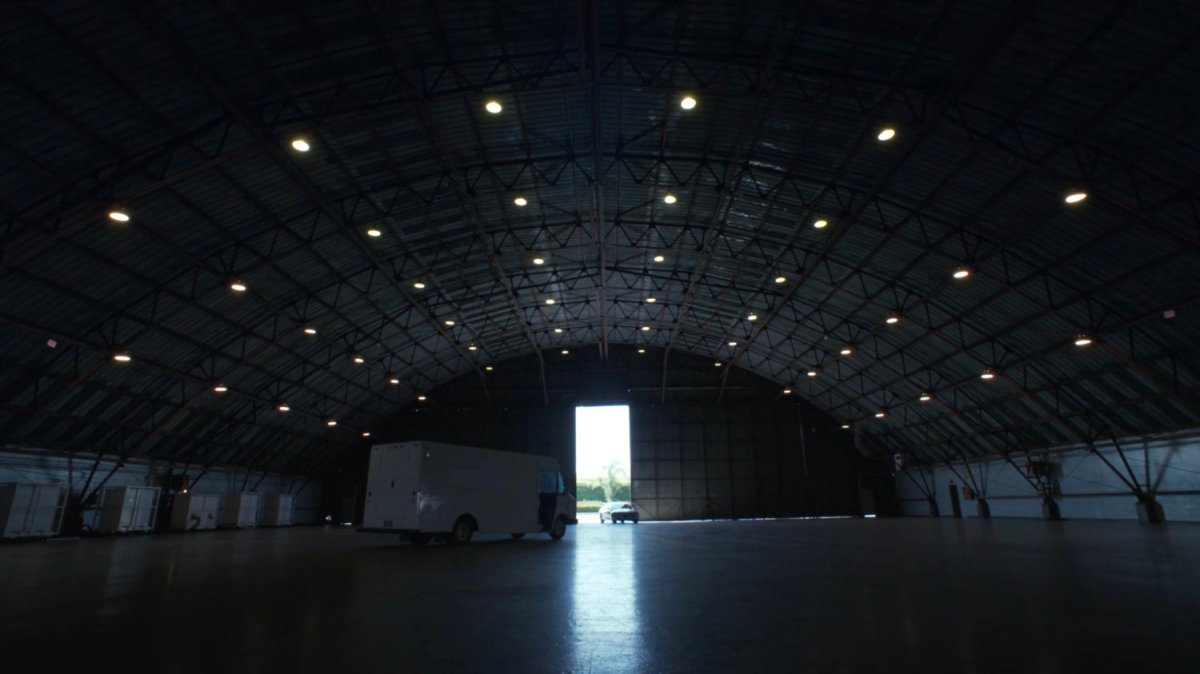 A van and car in an otherwise deserted airport hangar.