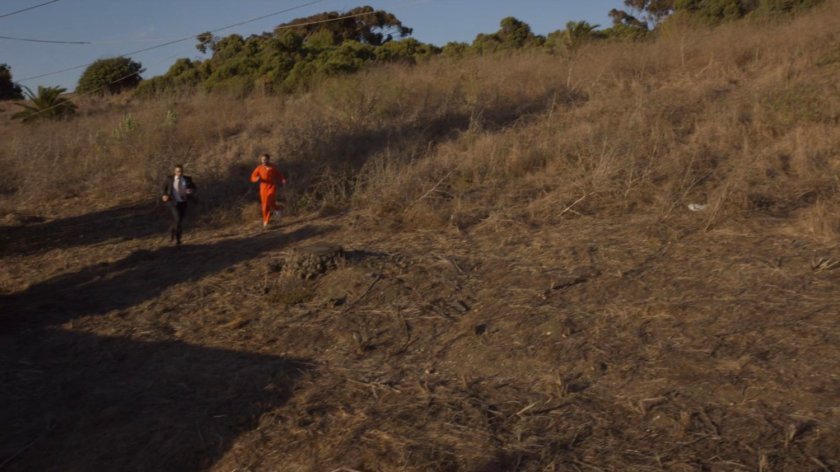 Hunter and Fitz running down a hillside outside a military base.