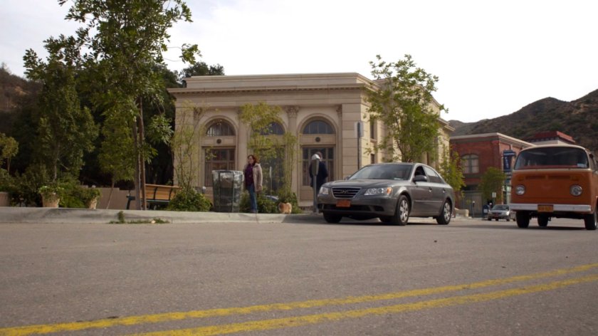 An orange van driving by a park in River's End.