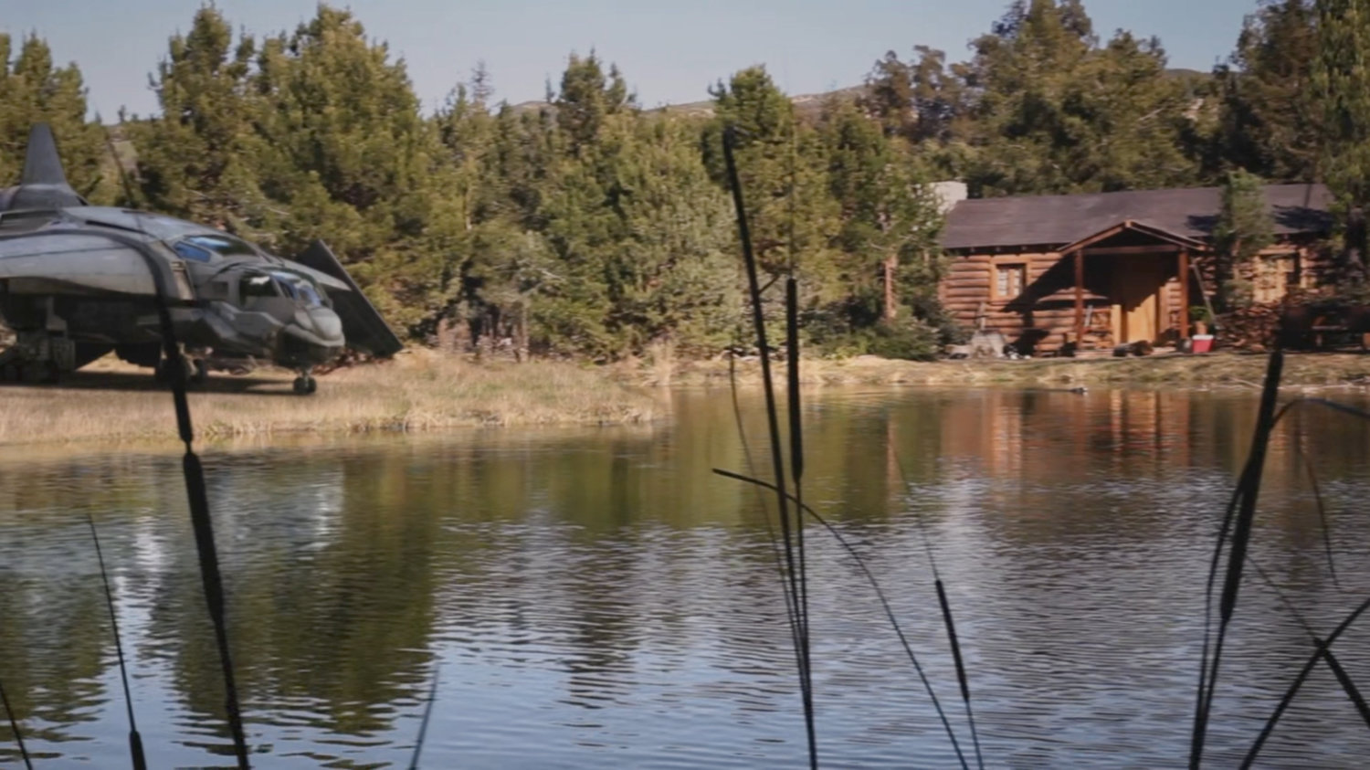 Exterior of Nick Fury's cabin by a lake, with a quinjet parked nearby.