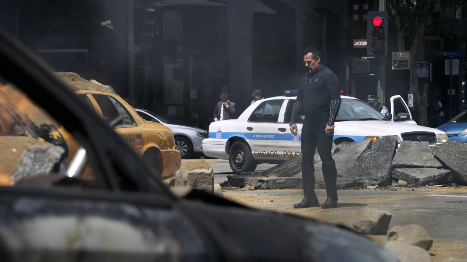Talbot standing in a Chicago intersection with debris and stopped vehicles around him.