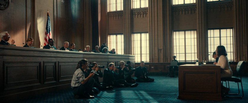 Val sitting in front of Senators in a Senate chamber.