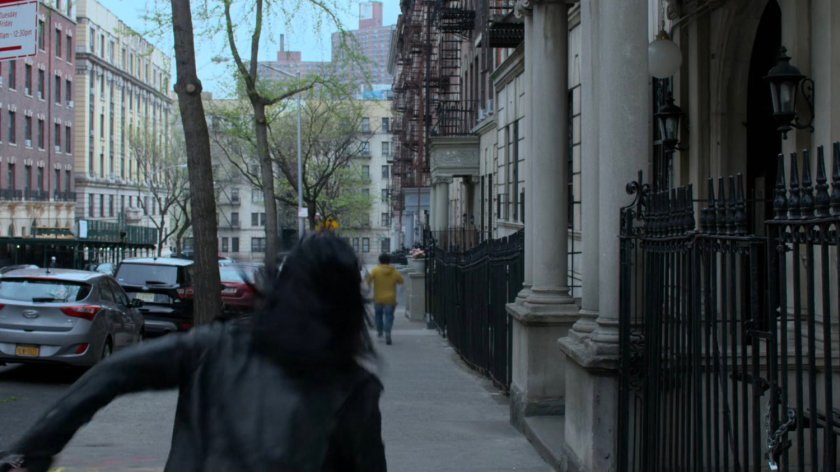 The Whizzer racing past Jessica on a sidewalk in front of the Alias Investigation building.