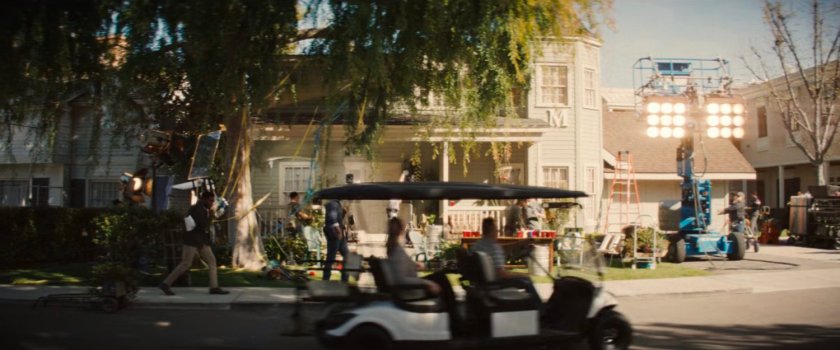 Simon Williams walking across the backlot of a Hollywood studio, past a house facade.