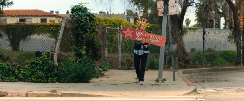 A woman holding a Hollywood Tour of Fame sign on a street corner.