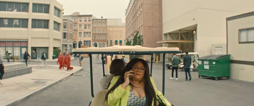 Janelle on a cell phone while riding in a golf cart around a Hollywood backlot.