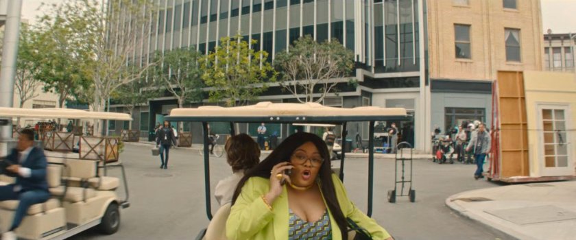 Janelle on a cell phone while riding in a golf cart around a Hollywood backlot.