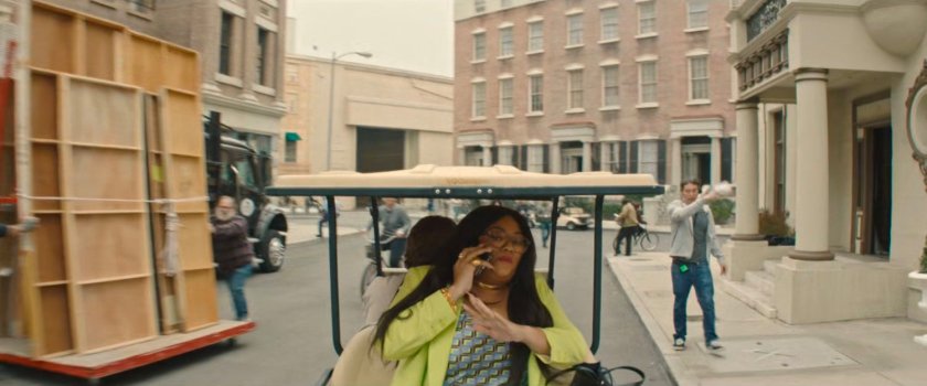 Janelle on a cell phone while riding in a golf cart around a Hollywood backlot.