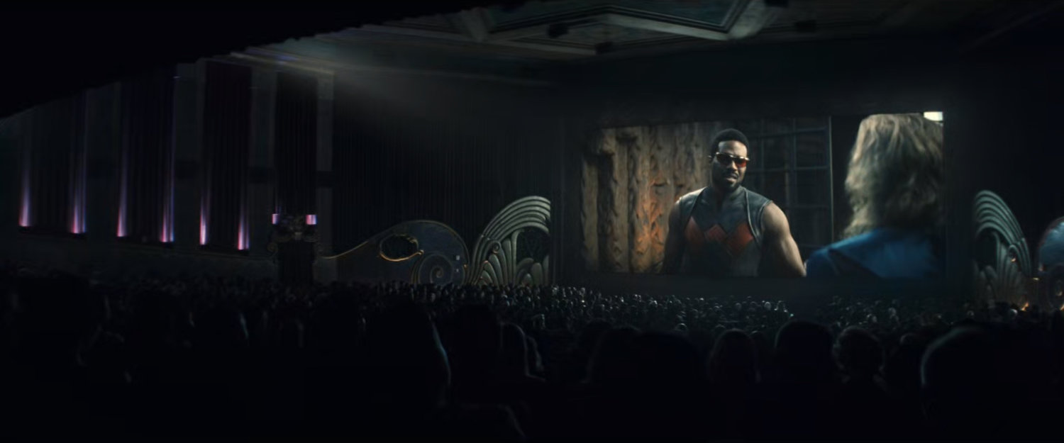 Interior of movie theater showing scene with Simon as Wonder Man.