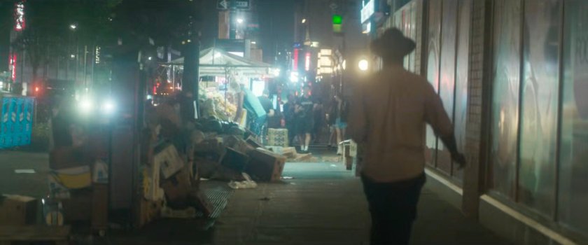 Interstitial: a pedestrian on a trash strewn sidewalk at night.