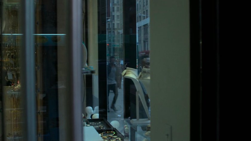 Malcolm walking along a sidewalk outside a jewelry store.