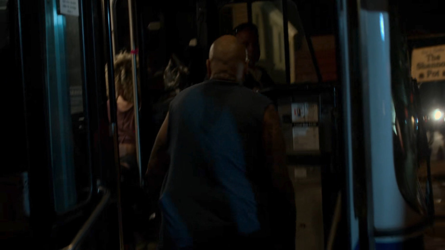 A man stepping onto a bus at night.