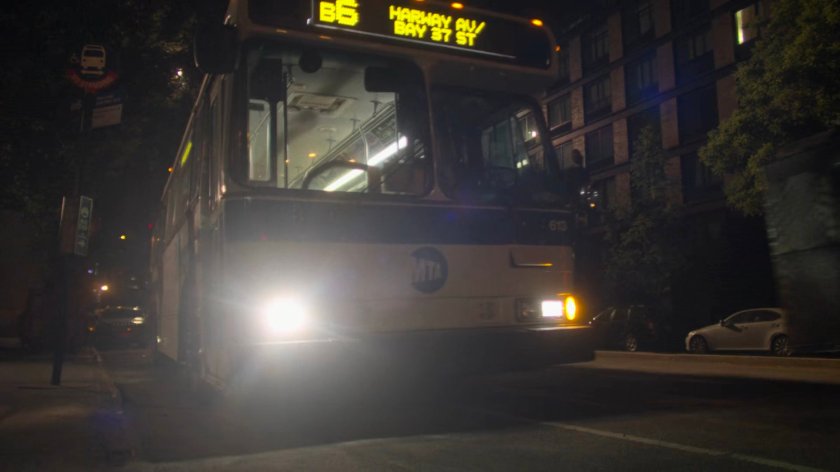 A bus pulls up to the sidewalk at night.