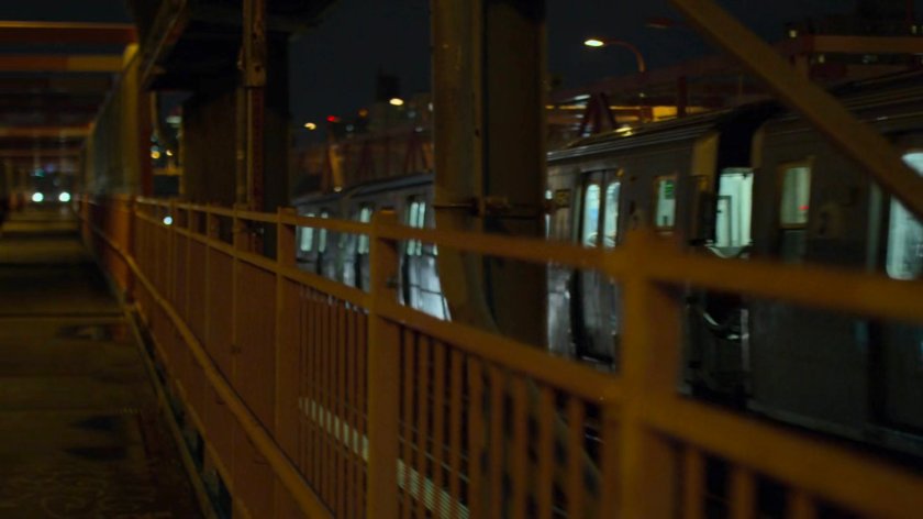 A subway train drives past fencing at a station.