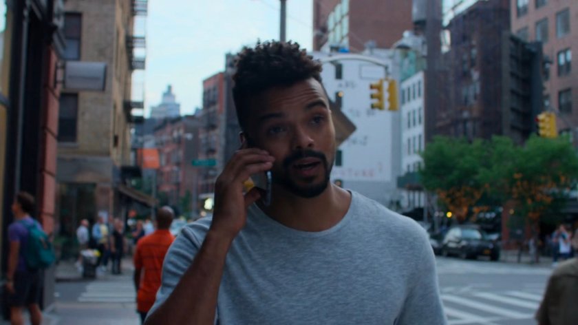 Malcolm searching for Jessica while on the phone along a sidewalk.