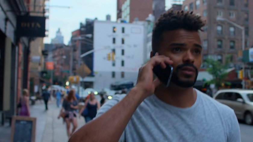 Malcolm searching for Jessica while on the phone along a sidewalk.