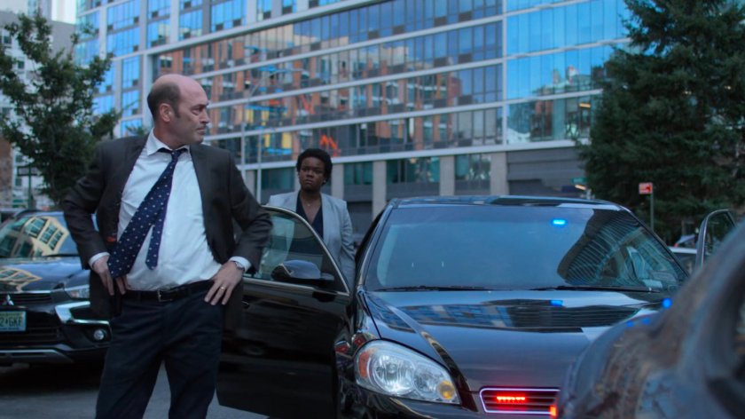 Detectives Costa and Sunday standing outside his car.
