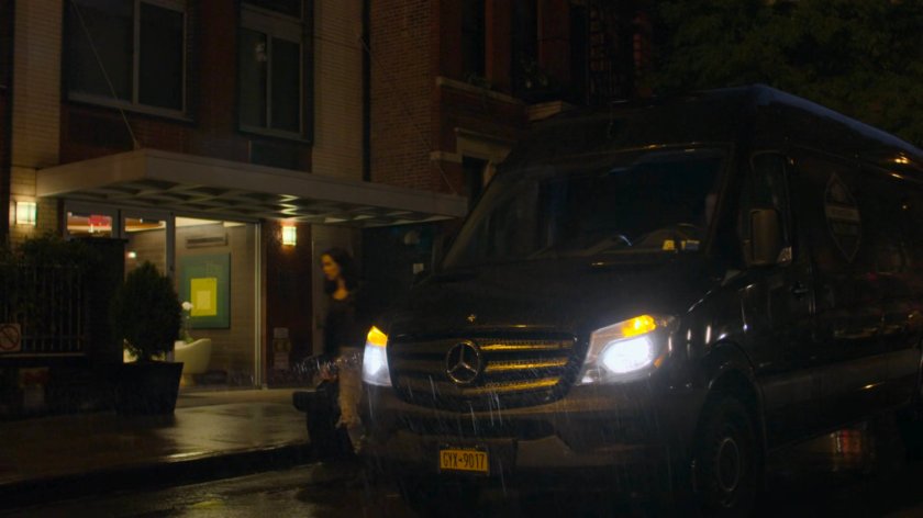 Jessica getting out of a mortuary van outside Trish's apartment building.