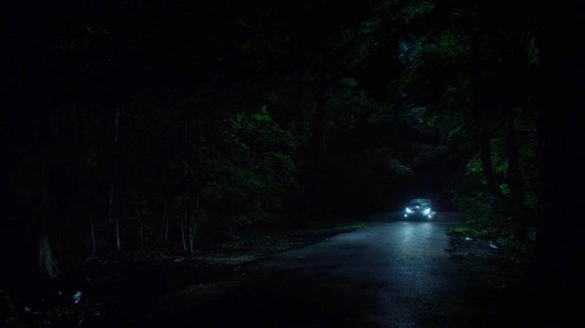 A car on a dark road lit by headlights.