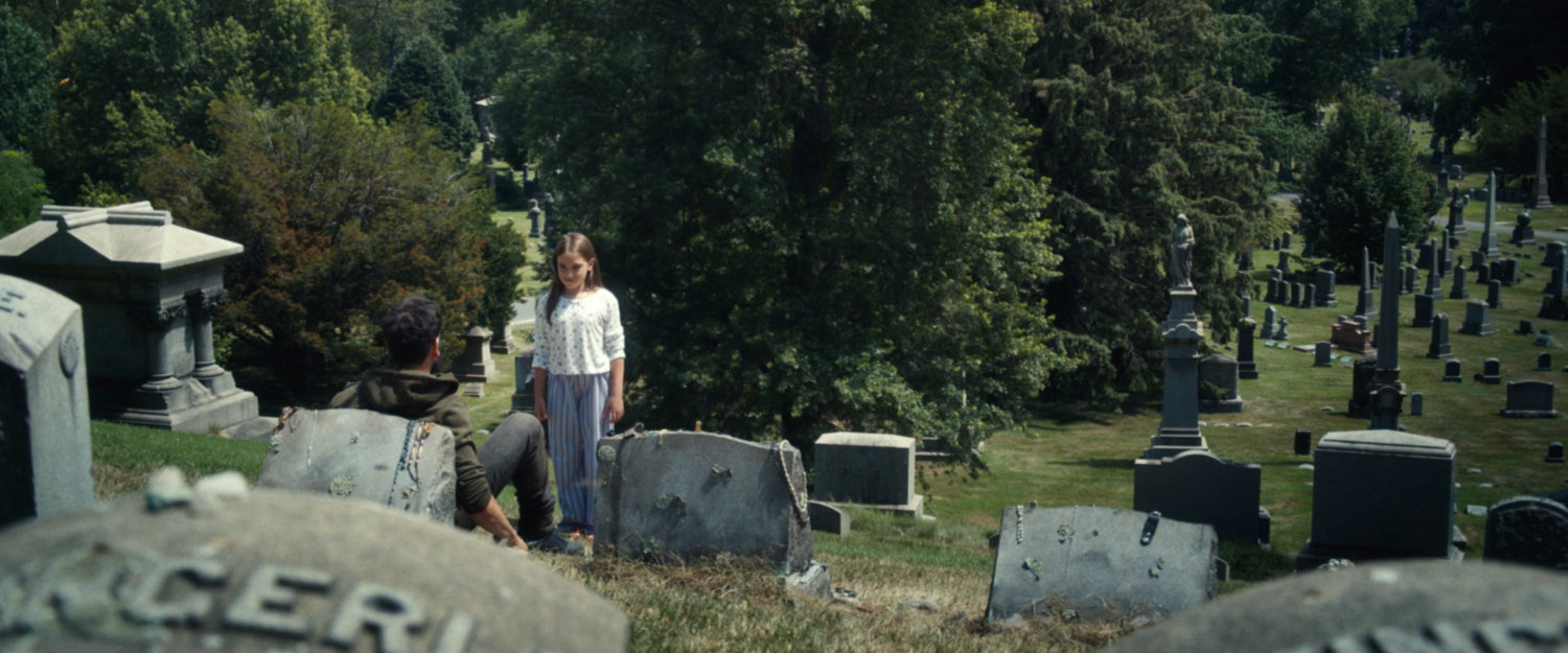 The ghost of Frank's daughter visits him as he sits by the gravestones of his family at a cemetery.