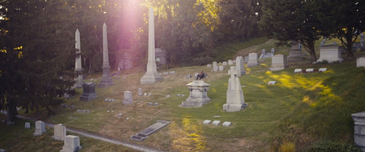 Frank sits by the gravestones of his family at a cemetery.
