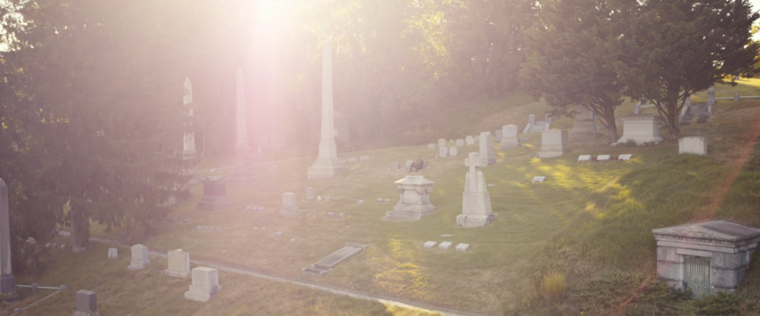 Frank sits by the gravestones of his family at a cemetery.