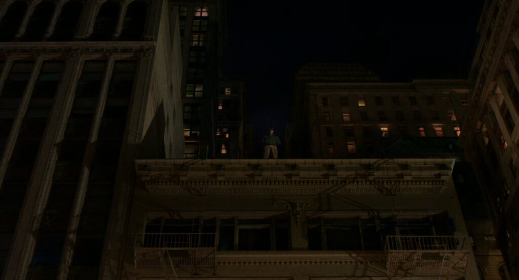 Flint standing on a rooftop across from the Alcove Theater, watching Cat in her apartment.